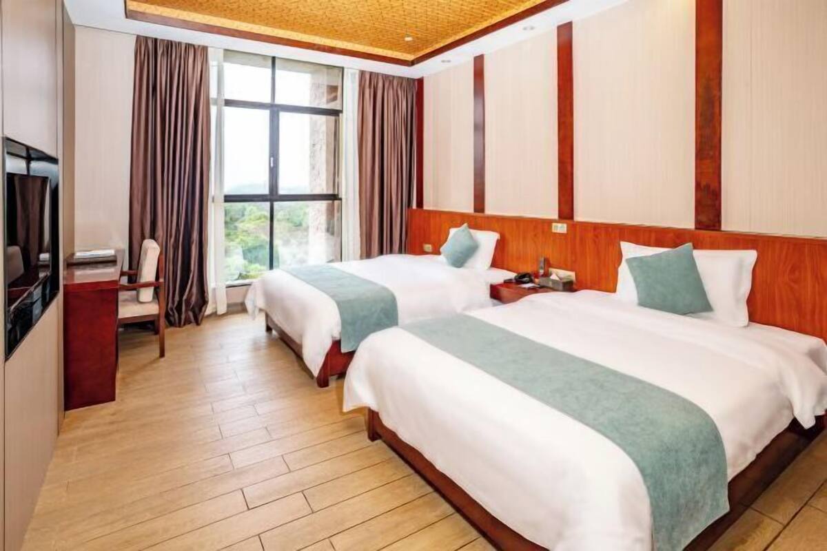 A hotel room with two beds, a TV, a desk, and a window with curtains.