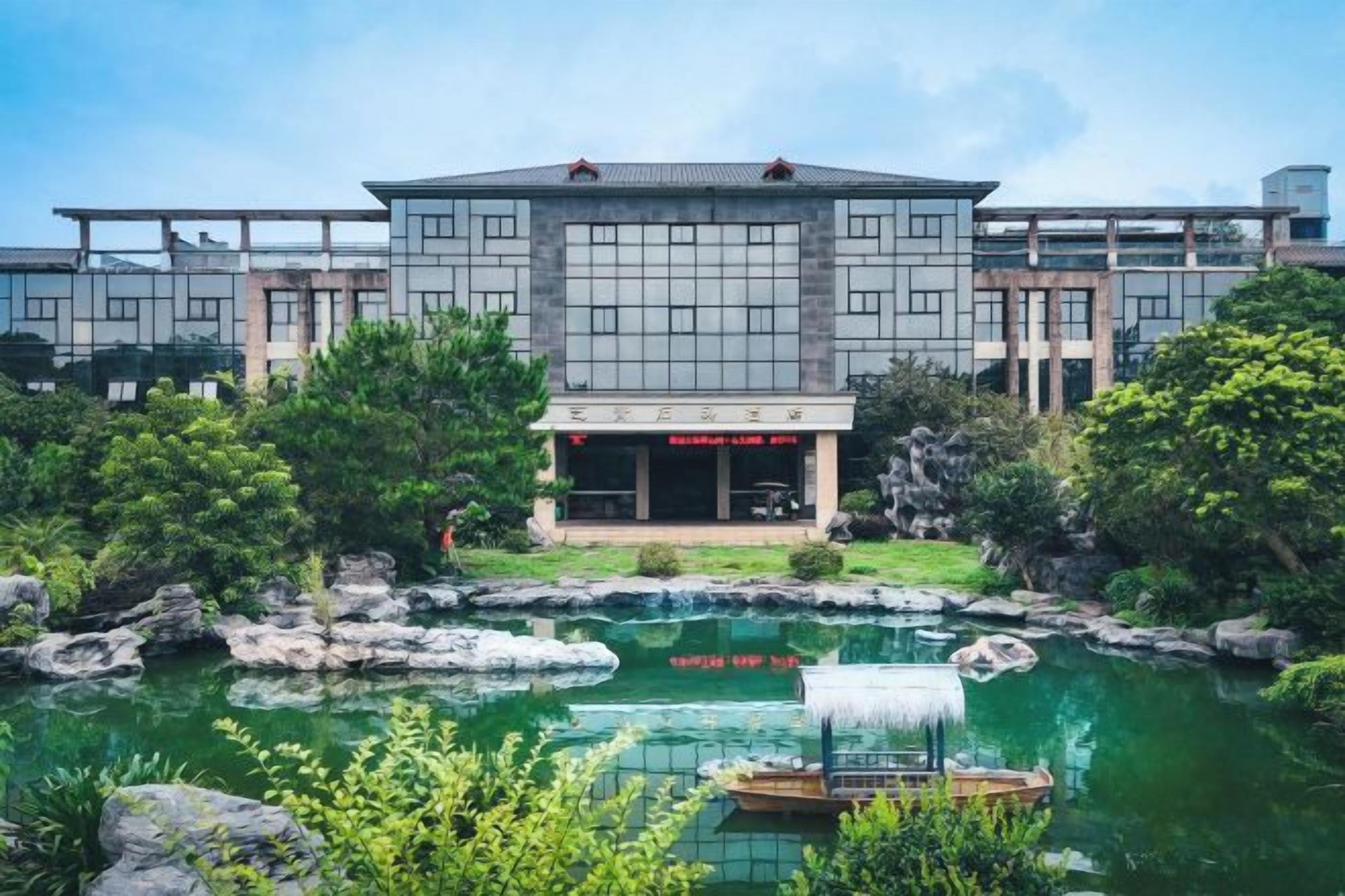 A modern building with a central entrance, a landscaped garden with a pond, and a small boat.