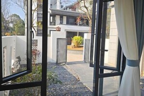 A modern building with a gated entrance, a small garden area, and a view of a residential building in the background. - Stone Hotel (Yingde)