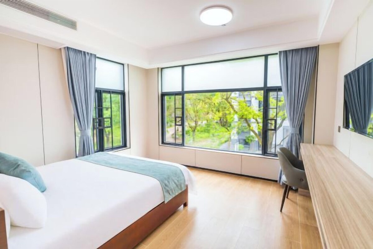 A bedroom with a bed, a desk, and large windows.