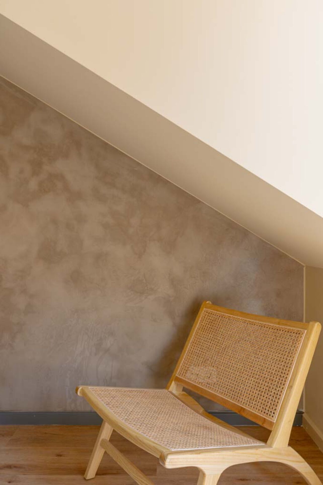 A corner of a room with a sloped ceiling and a wooden chair with a woven seat and backrest.
