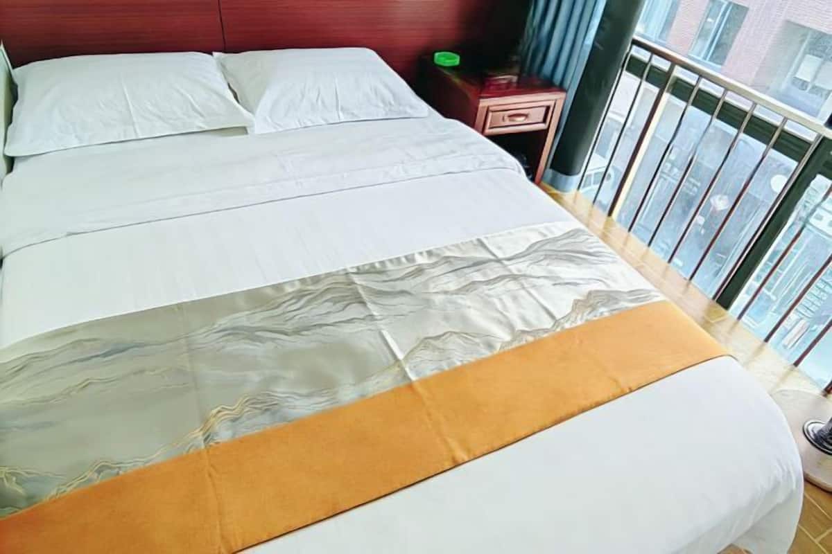 A bed with white bedding and a patterned blanket, a wooden headboard, and a nightstand with a green object.