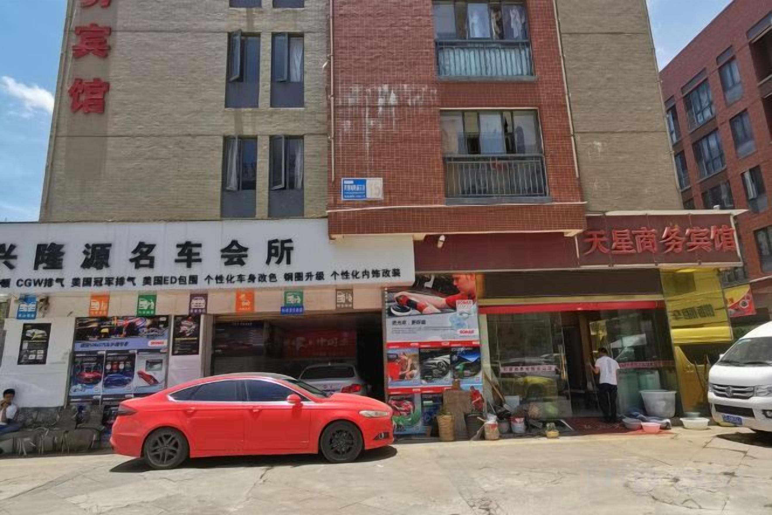 Un immeuble à plusieurs étages abritant divers commerces au rez-de-chaussée, notamment une concession automobile et un magasin avec un auvent rouge.