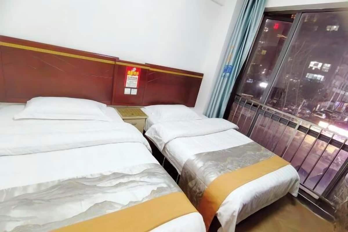 A hotel room with two beds, a wooden headboard, a window with a view of the city, and a sign on the wall.