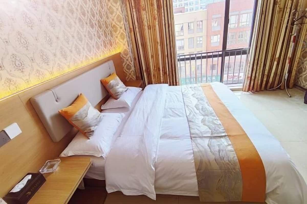 A hotel room with a large bed, a bedside table, a nightstand, and a view of buildings through the window.