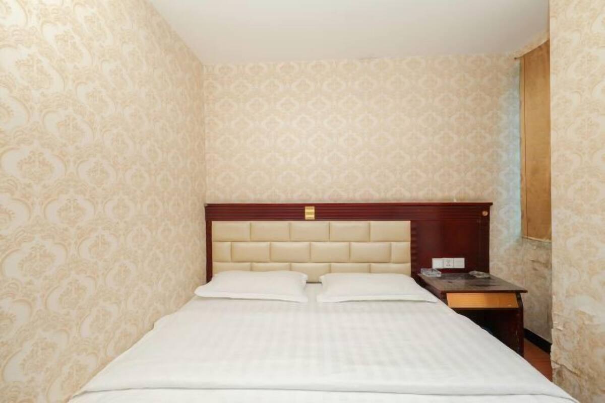 A hotel room with a bed, a wooden headboard, a nightstand, and patterned wallpaper.