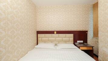 A hotel room with a bed, a wooden headboard, a nightstand, and patterned wallpaper.