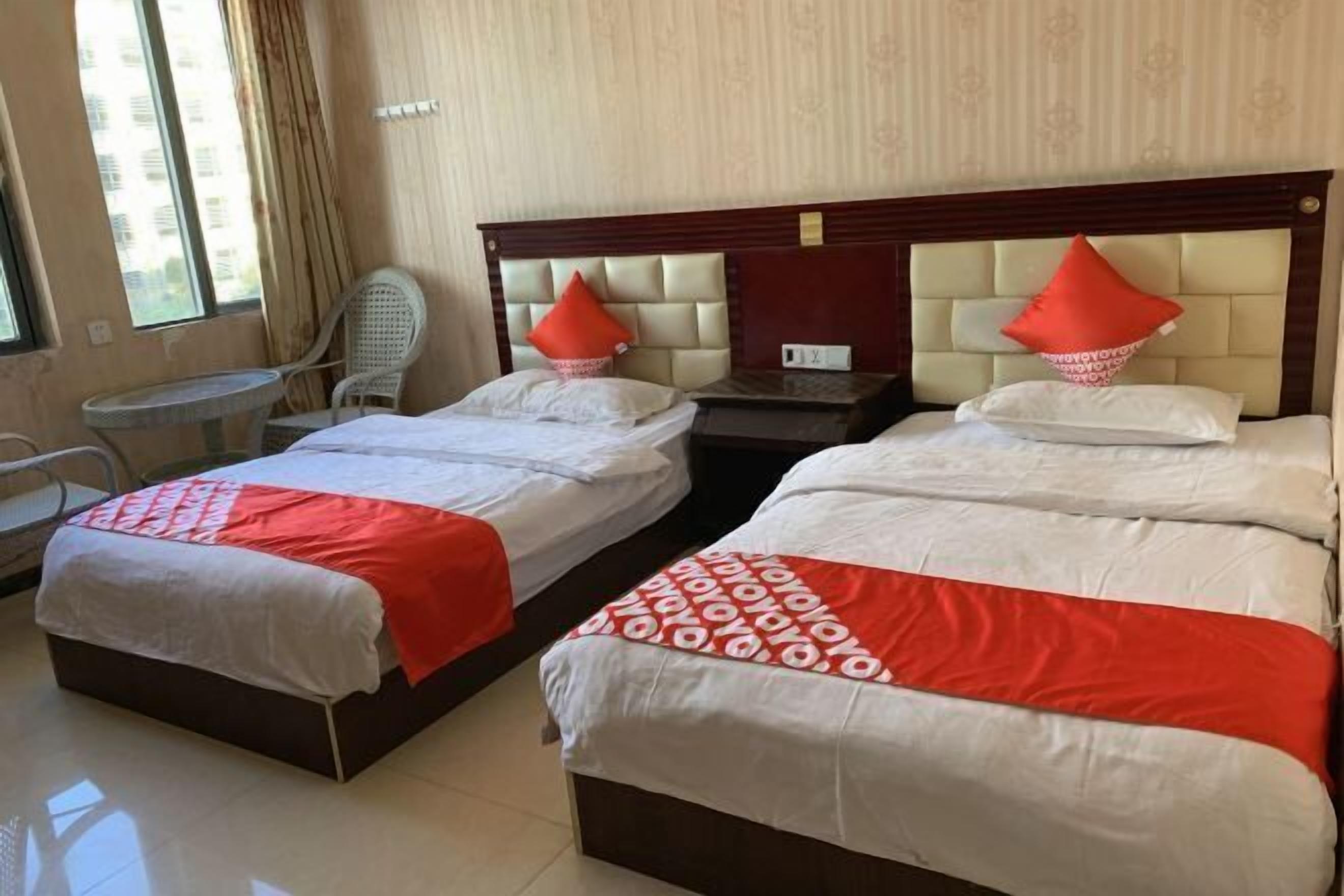 A hotel room with two beds, each with a red and white bedspread, a wooden headboard, and a small table with a chair.