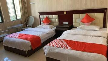 A hotel room with two beds, each with a red and white bedspread, a wooden headboard, and a small table with a chair.