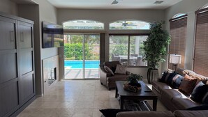 A spacious living room with a large sliding glass door leading to a pool, a ceiling fan, and a comfortable seating area with a coffee table. - Desert Getaway in Indio with private pool & golf course  (Indio)