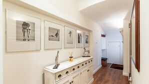 A hallway with framed artwork on the wall, a wooden cabinet with drawers, and a door at the end.