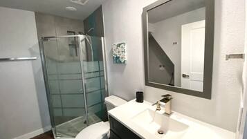 A modern bathroom with a glass shower enclosure, a white toilet, and a white sink with a large mirror above it.
