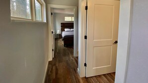 Un pasillo estrecho con suelo de madera que conduce a un dormitorio con cama y mesita de noche.
