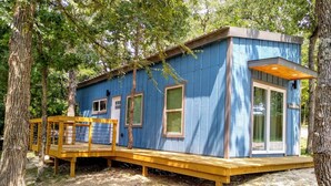 Una cabaña azul con terraza de madera, rodeada de árboles.