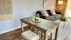 Una mesa de comedor de madera con un banco, una planta en maceta y un adorno de macramé colgado en la pared.