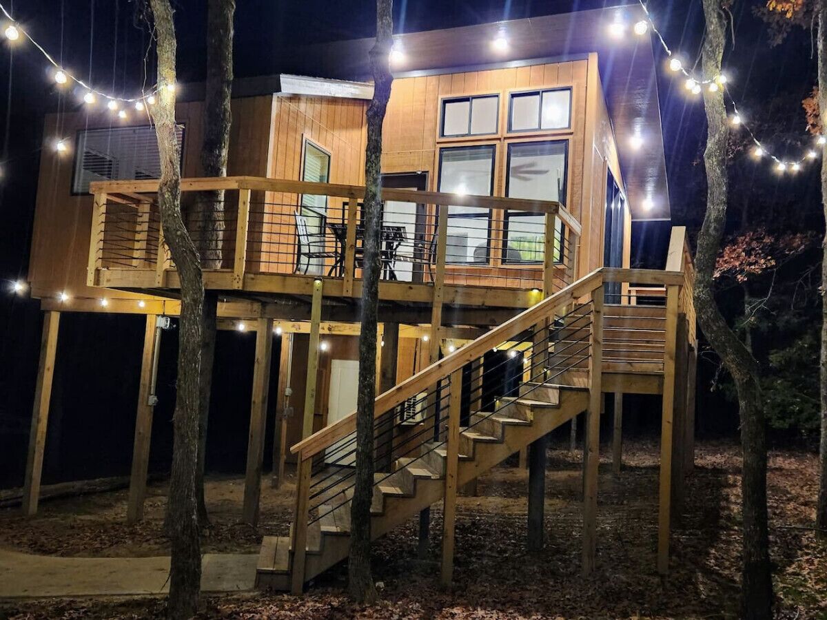 A wooden cabin with a staircase and deck, surrounded by trees.