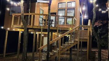 A wooden cabin with a staircase and deck, surrounded by trees.
