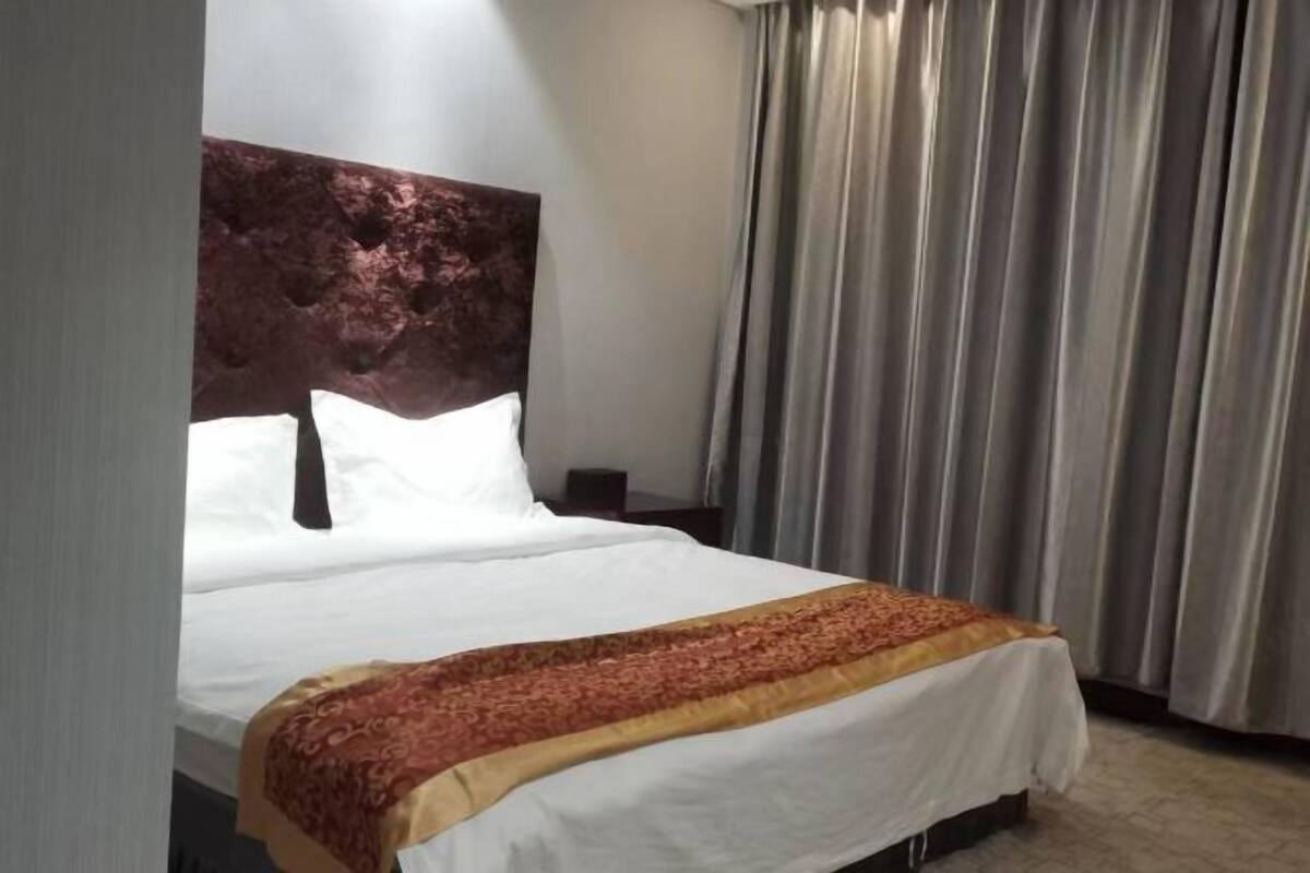 Una habitación de hotel con una cama grande, cabecera y cortina.
