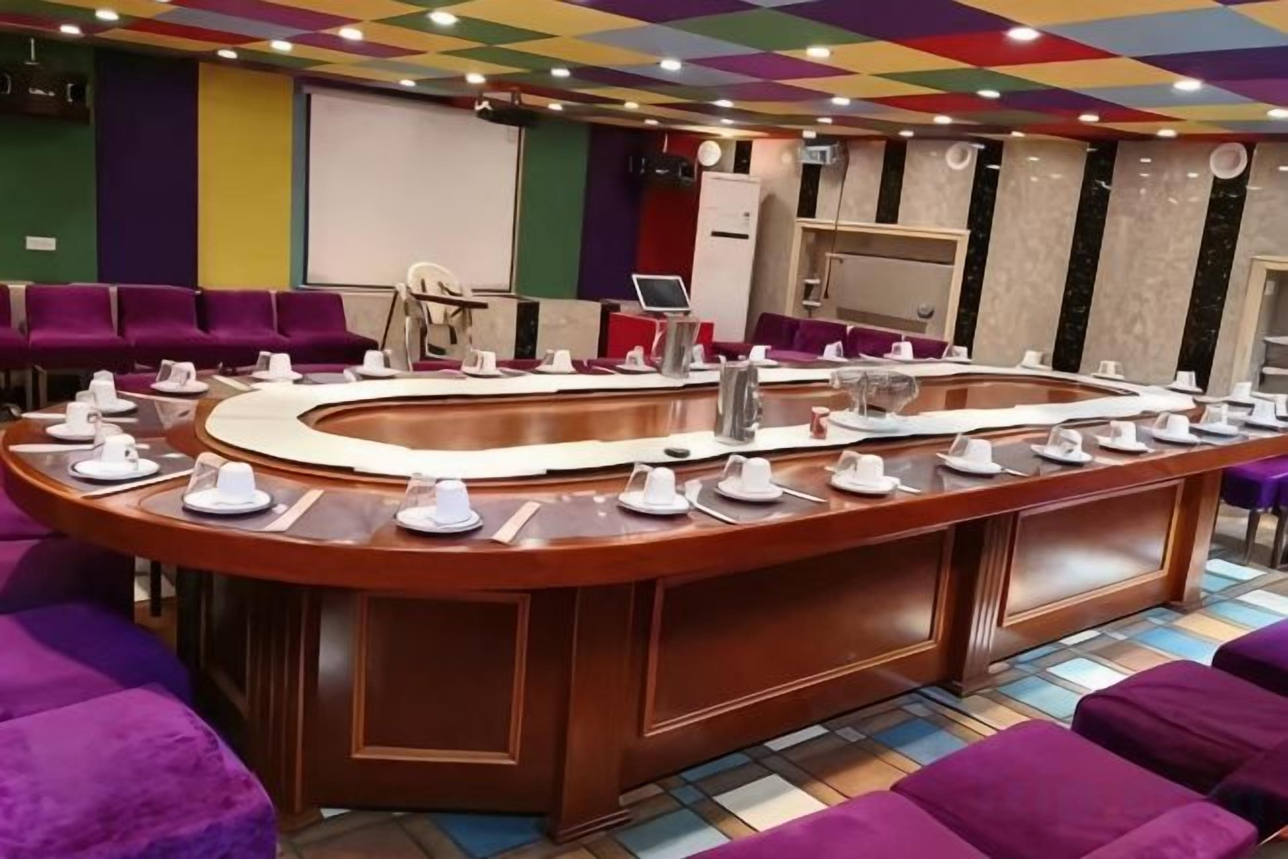Sala de conferência com uma mesa central, cadeiras e uma tela de projeção.