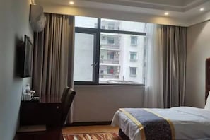 A hotel room with a bed, a desk, a chair, and a window with a view of a building. - Yanduhe Hotel (Badong)