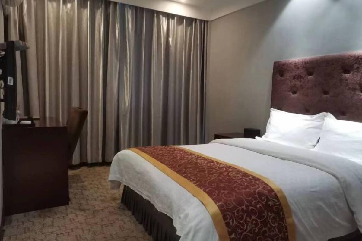 Una habitación de hotel con una cama grande, cabecero, escritorio y cortina.