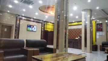 A hotel lobby with seating, a reception desk, a television screen, and a digital display.