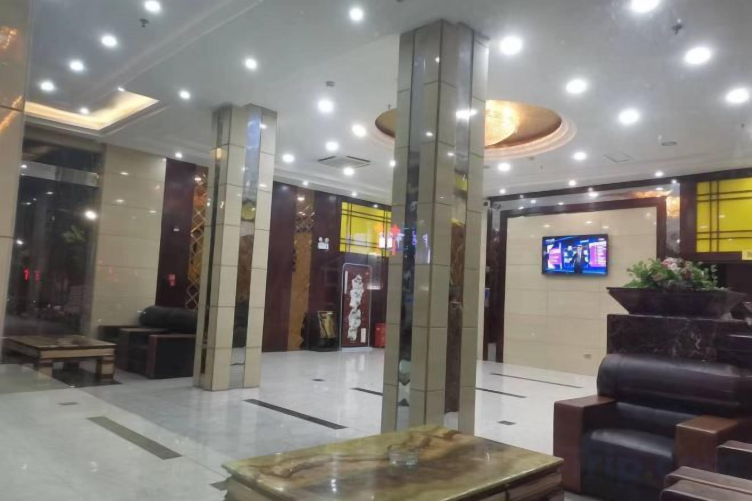 A hotel lobby with a reception desk, seating area, and a television screen.