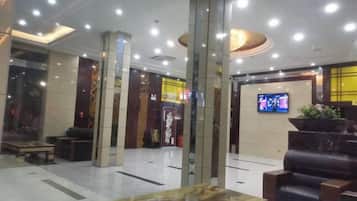 A hotel lobby with a reception desk, seating area, and a television screen.