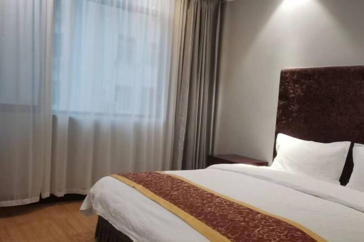 Una habitación de hotel con una cama grande, piso de madera y una ventana con cortinas translúcidas.