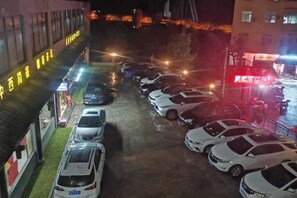 A parking lot with multiple cars parked in rows, a building with illuminated signage, and a street with lights in the background. - Yanduhe Hotel (Badong)