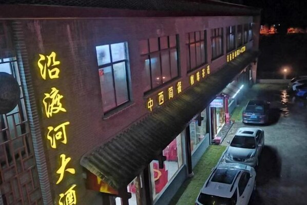 A building with a sign in a foreign language, a covered walkway, and parked cars.