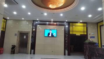 A lobby with a reception desk, a television screen, and a large chandelier.