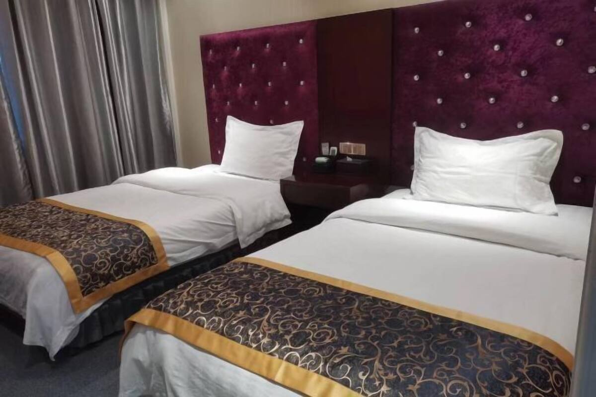 Habitación de hotel con dos camas, cada una con cabecero, ropa de cama blanca y colcha estampada.