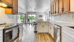 A kitchen with wooden cabinets, a stainless steel dishwasher, and a large window overlooking greenery. - Private Island Getaway in Roanoke Rapids w/ Grill! (Roanoke Rapids)