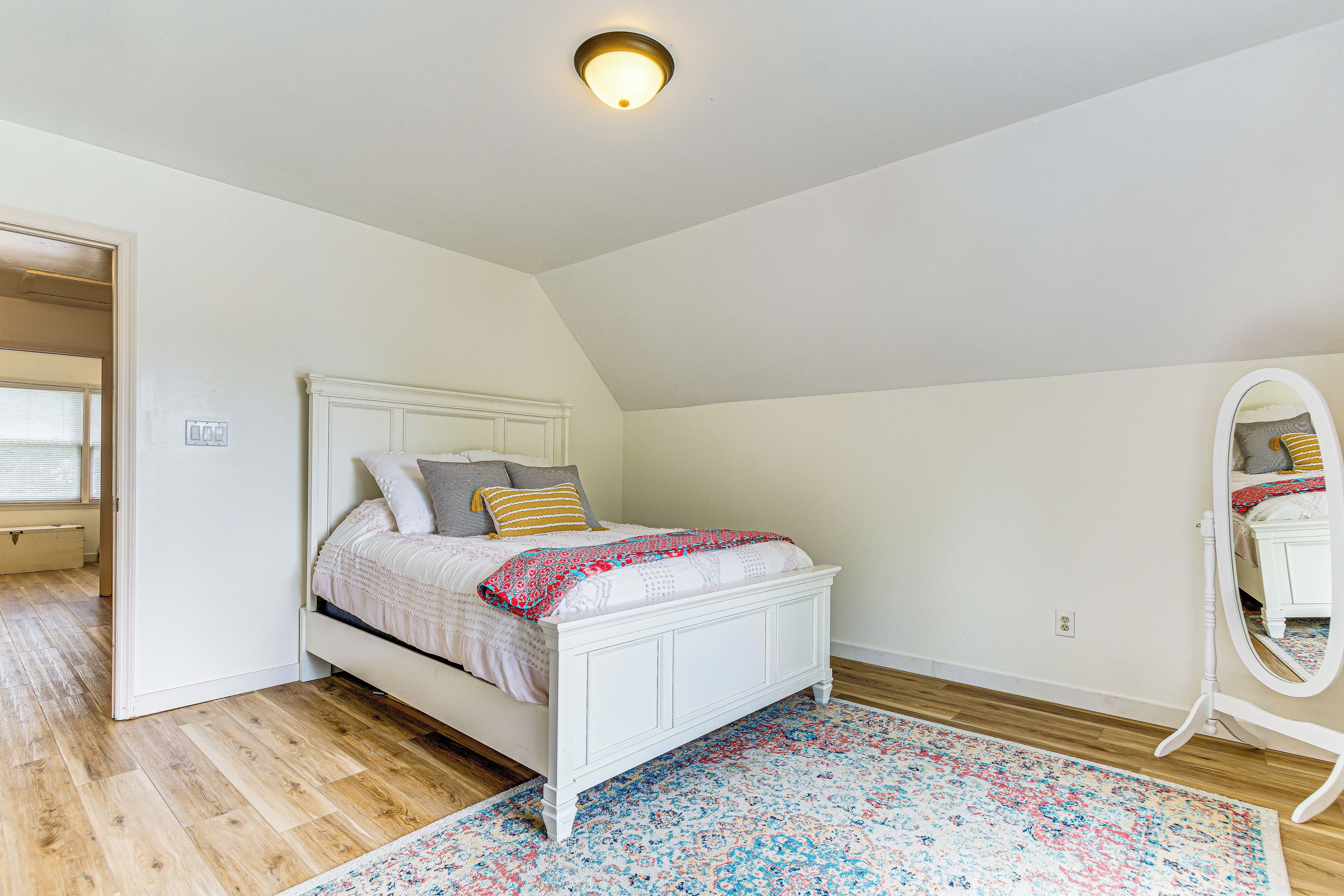 Un dormitorio con cama blanca, alfombra estampada, cómoda blanca y espejo.