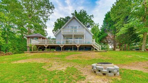 A two-story house with a balcony, surrounded by a grassy yard and trees. - Private Island Getaway in Roanoke Rapids w/ Grill! (Roanoke Rapids)