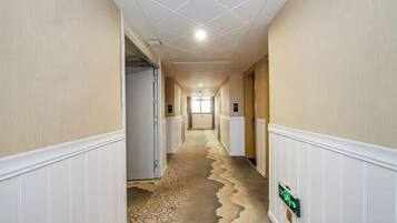 Un couloir d’hôtel avec un tapis à motifs, des lambris blancs et un panneau vert indiquant la sortie de secours.