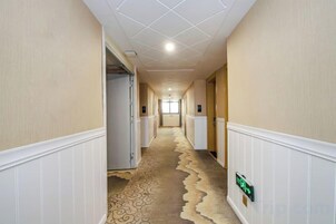 Un pasillo de hotel con alfombra estampada, paneles blancos y un letrero de salida de emergencia verde.