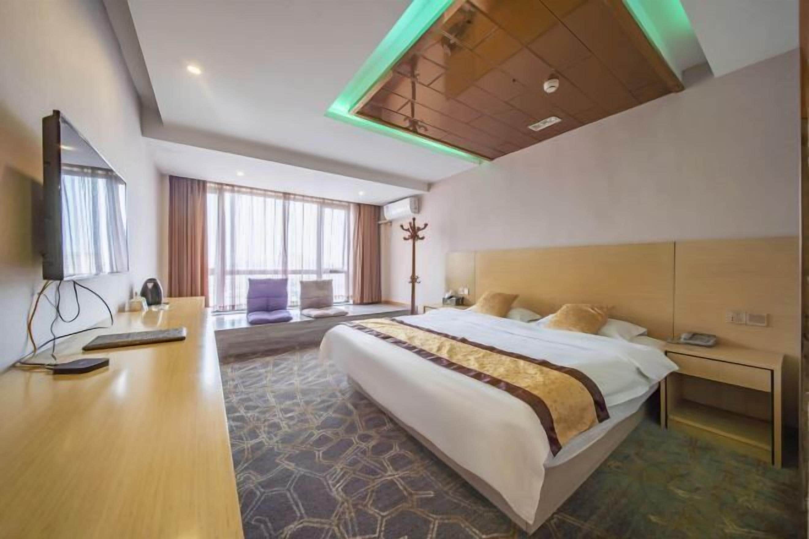 A hotel room with a bed, bedside table, lamp, and a large window.