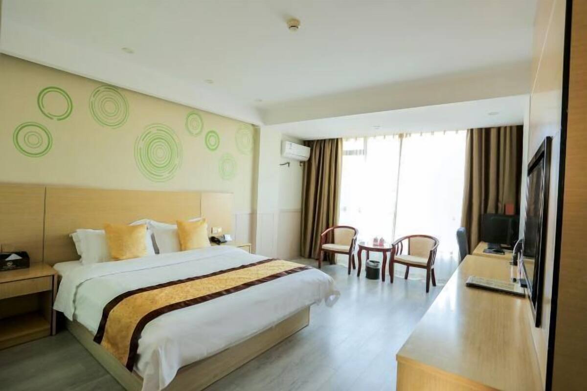 A hotel room with a bed, a desk, a chair, a TV, and a window with curtains.