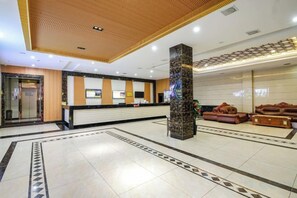Un hall d’hôtel comprenant un comptoir d’accueil, un espace salon et un pilier décoratif.