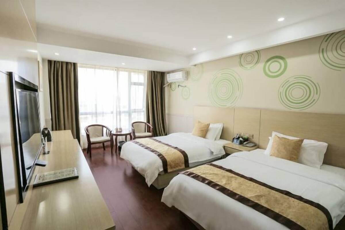 A hotel room with two beds, a desk, a chair, a TV, and a window with curtains.