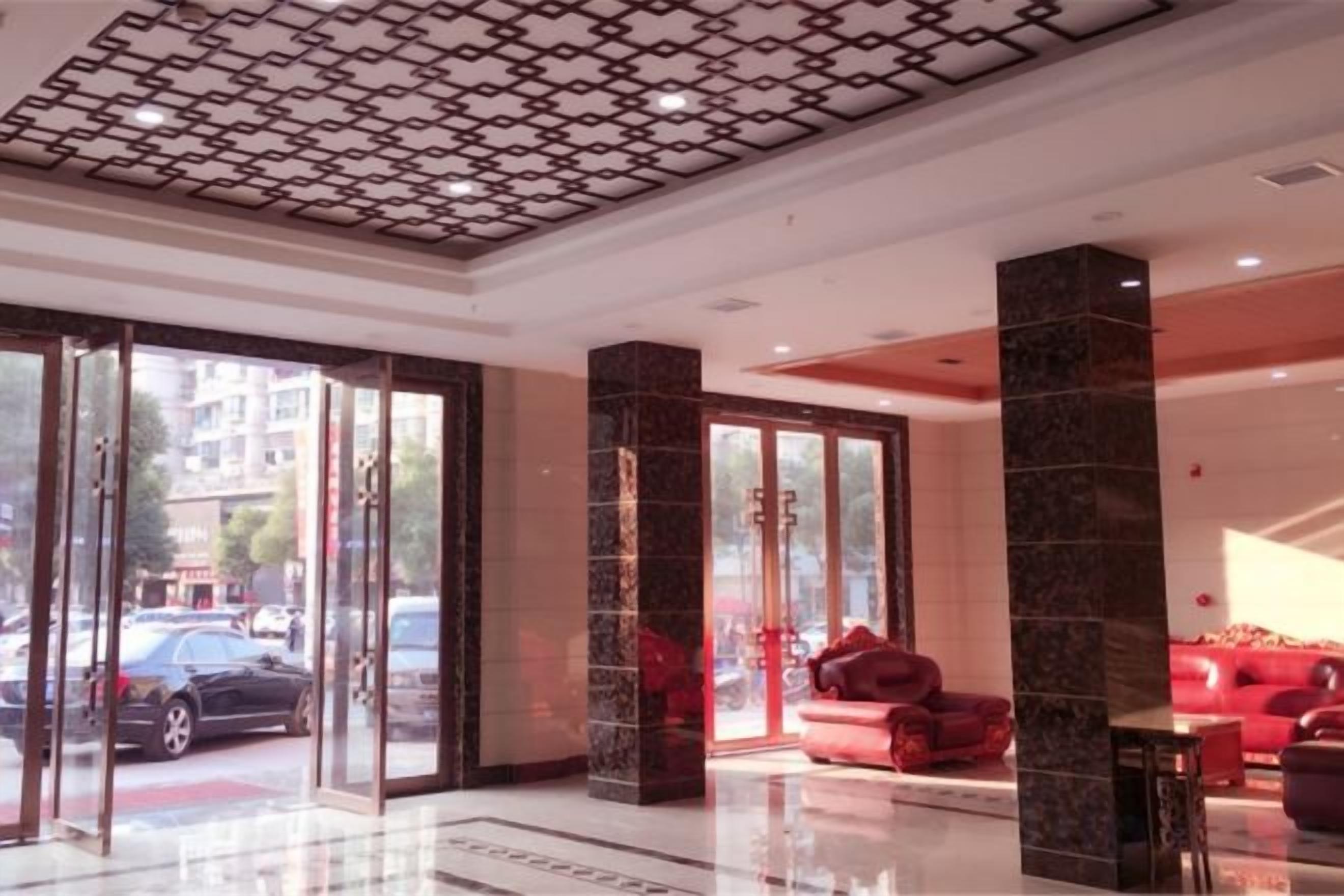 Un hall de hotel con entrada de vidrio, asientos rojos y techo estampado.