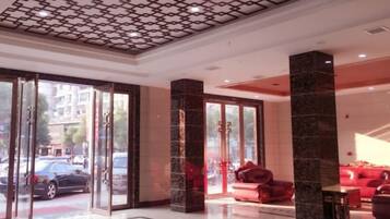 Un hall de hotel con entrada de vidrio, asientos rojos y techo estampado.