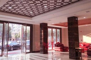 Un hall de hotel con entrada de vidrio, asientos rojos y techo estampado.
