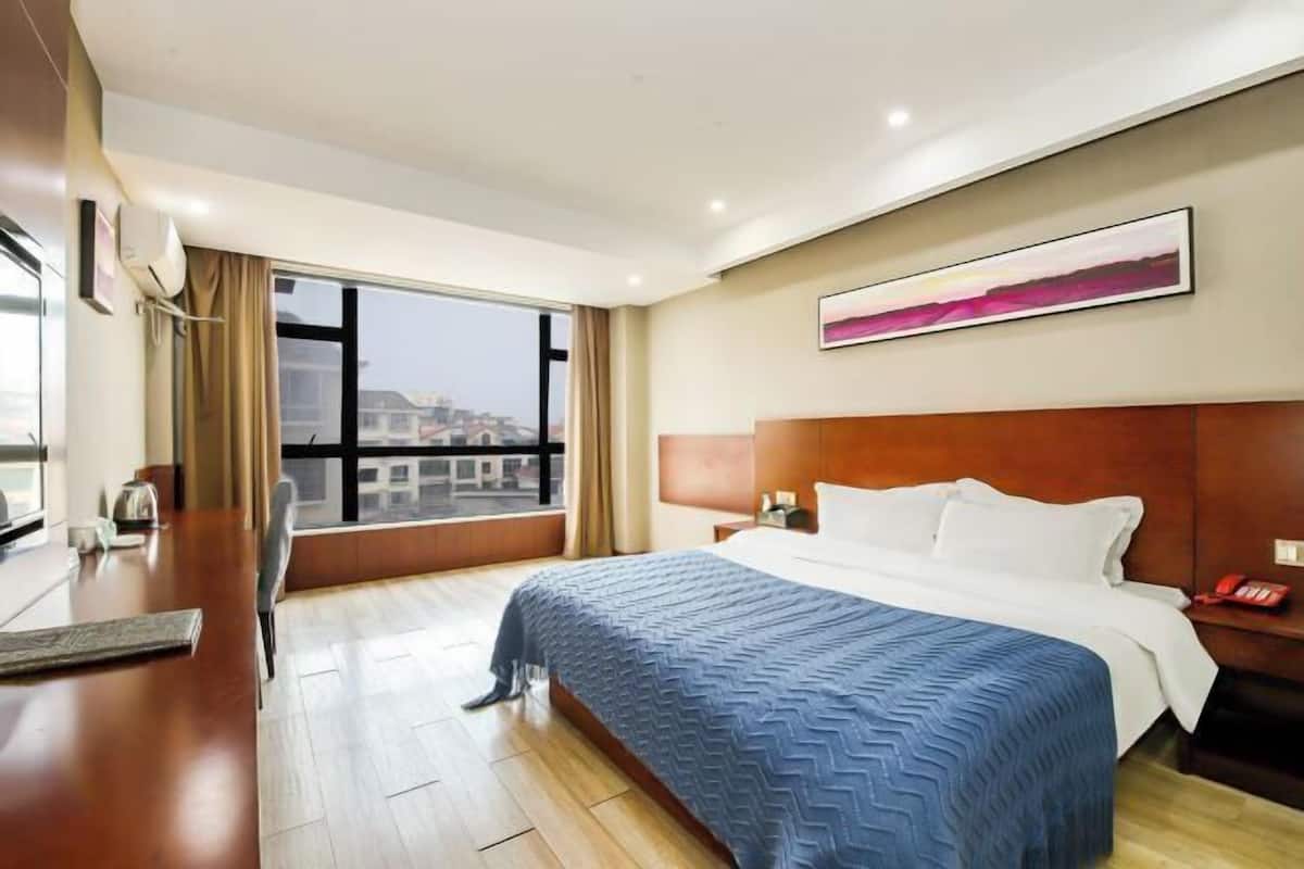 A hotel room with a large bed, a desk, and a window with a city view.