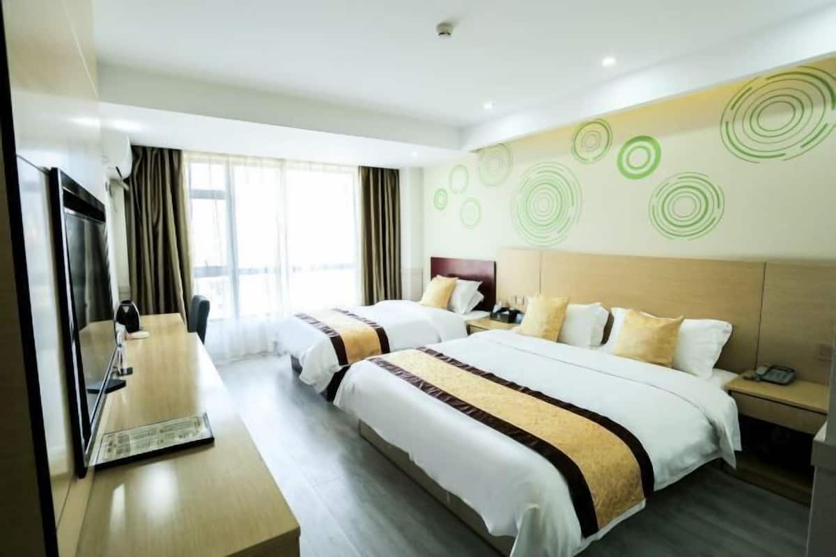 A hotel room with two beds, a desk, a TV, and a wall with circular patterns.