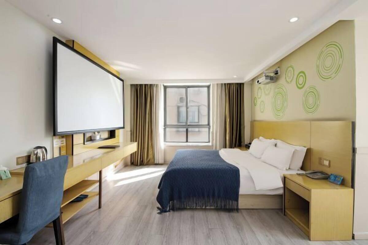 A hotel room with a bed, a desk, a chair, a television, and a window.