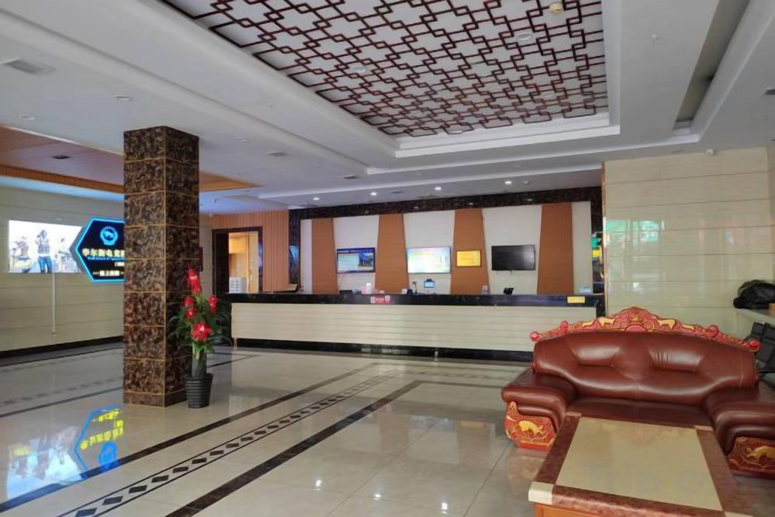 A hotel lobby with a reception desk, a large pillar, a sofa, and a patterned ceiling.