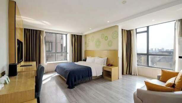 A hotel room with a bed, a desk, a chair, a TV, and large windows. - The Wall Street Holiday Hotel (Yichun)